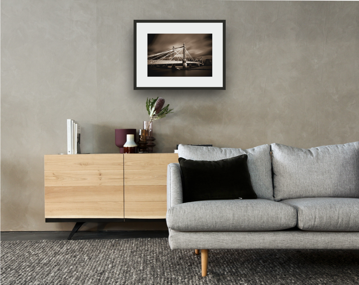 Framed and mounted photograph of Albert Bridge on the river Thames in South West London hanging on a wall above a sofa and cupboard
