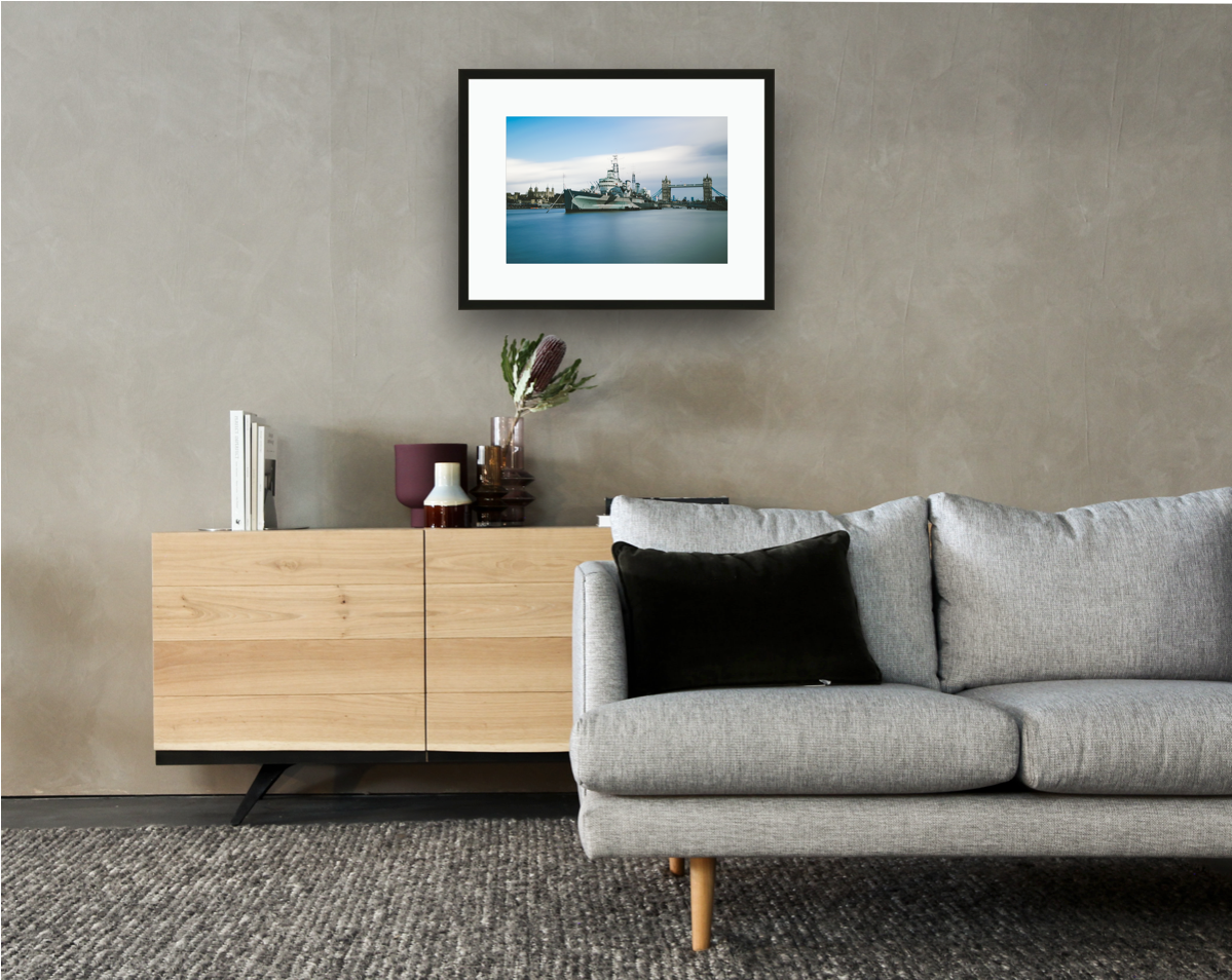 Framed and mounted photograph of hms belfast battleship on the river thames on southbank in the city of london hanging on a wall above a sofa and cupboard