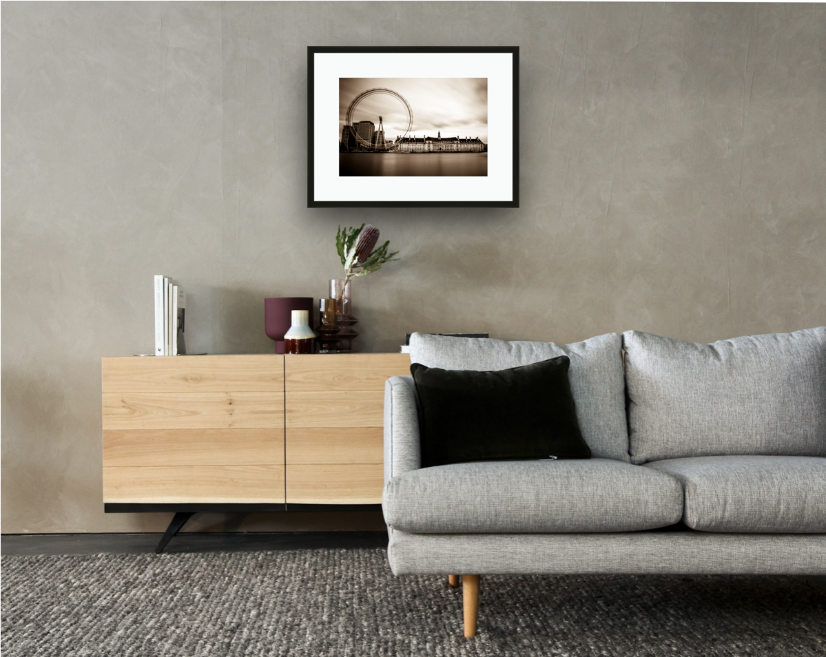 Framed and mounted photograph of London Eye & County Hall on the river Thames in central London hanging on a wall above a sofa and cupboard