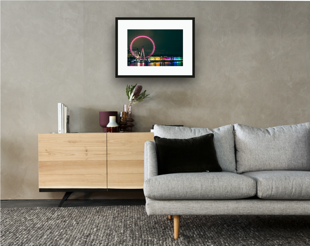 Framed and mounted photograph of London Eye & County Hall At Night on the river Thames in South West London hanging on a wall above a sofa and cupboard