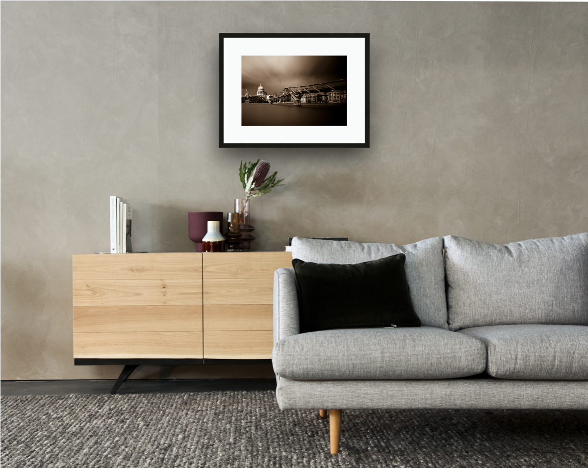 Framed and mounted photograph of Millennium Bridge and St Pauls Cathedral on the river Thames in the city of London hanging on a wall above a sofa and cupboard