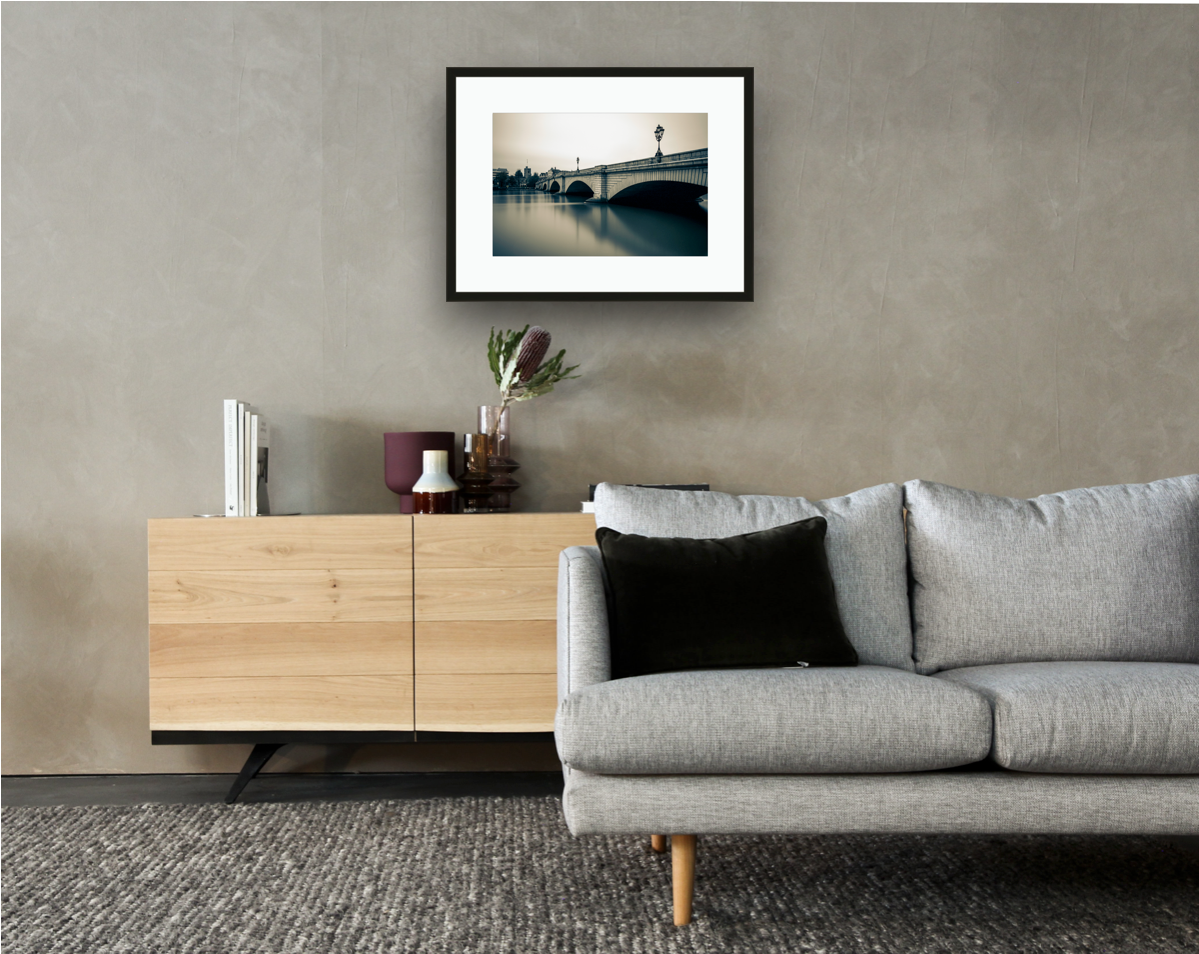 Framed and mounted photograph of putney bridge on the river thames in south west london hanging on a wall above a sofa and cupboard