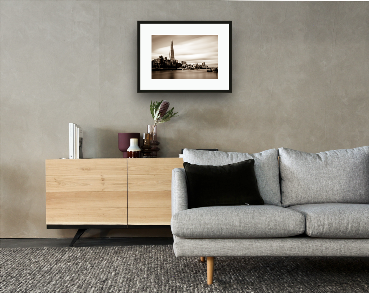 Framed and mounted photograph of The Shard on the river Thames in London hanging on a wall above a sofa and cupboard