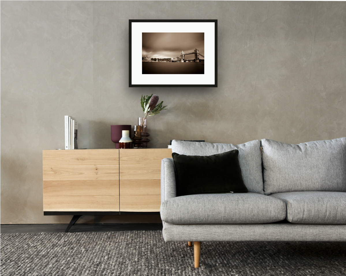 Framed and mounted photograph of Tower Bridge & Tower of London on the river Thames in central London hanging on a wall above a sofa and cupboard